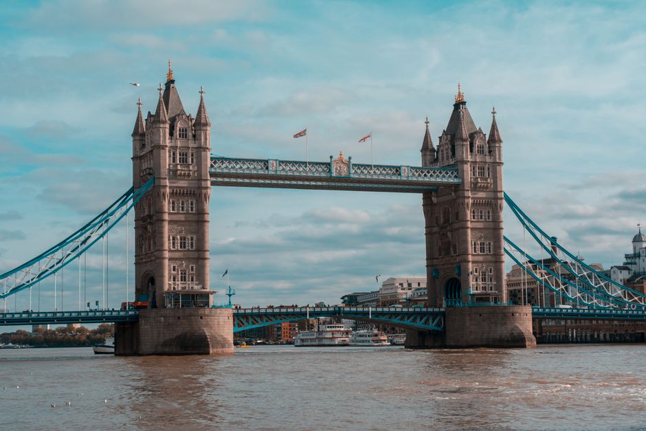 A wide view of Tower Bridge spanning the River Thames in London, with the historic bascule bridge's two towers featuring intricate Gothic-style architecture. The river below appears calm with a few bo